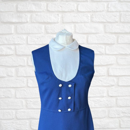 Blue dress with white collar on a mannequin against a white brick wall background