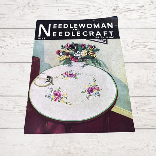 Magazine cover titled 'Needlewoman and Needlecraft' with a floral design on a wooden surface.
