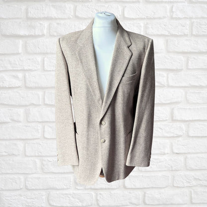 A light beige textured herringbone blazer displayed on a white mannequin torso against a white brick wall background.