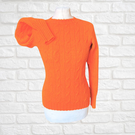 Orange cable knit sweater on a mannequin against a white brick wall background