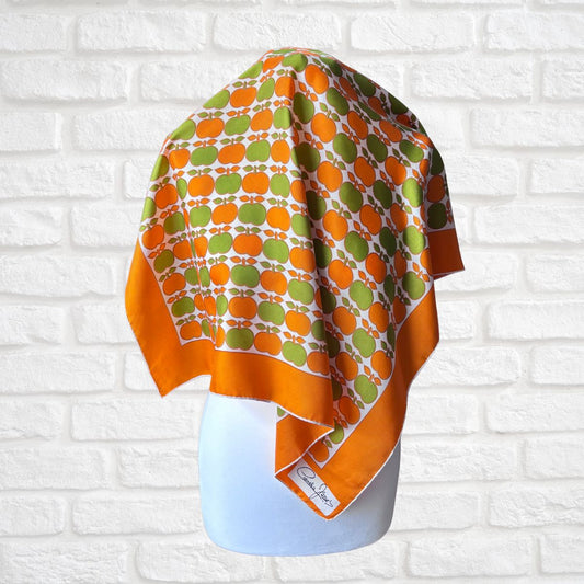 Orange and green patterned scarf on a mannequin against a white brick wall.