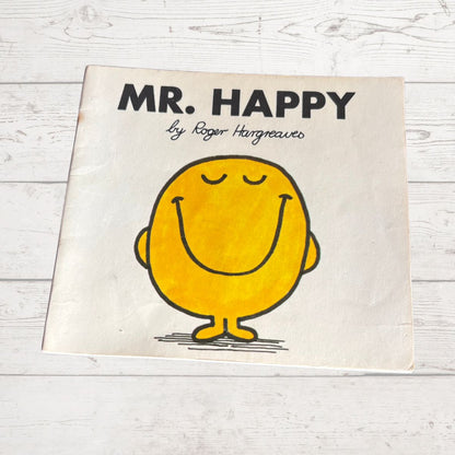 Book titled 'Mr. Happy' by Roger Hargreaves on a wooden surface