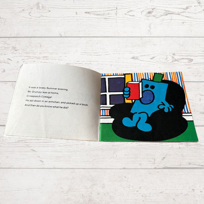 Open book with a colorful illustration of a blue character reading a book on a white wooden surface.