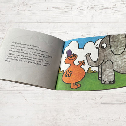Open book with illustrations of an orange creature and an elephant on a wooden surface