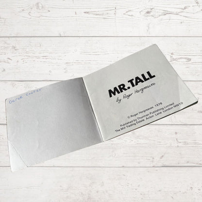 Open book titled 'MR. TALL' by Roger Hargreaves on a wooden surface