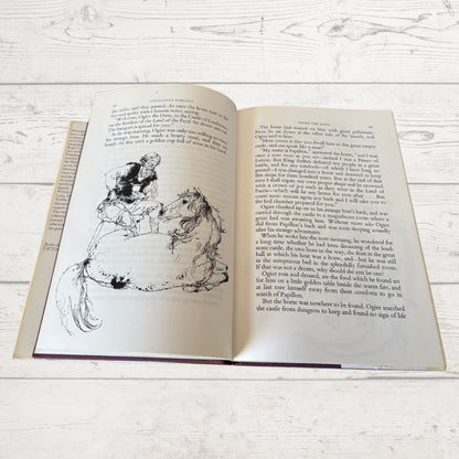 An open vintage book showing printed text and a black ink illustration of two figures, photographed on a light whitewashed wooden surface.