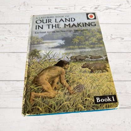 A vintage hardcover book titled 'Our Land in the Making: earliest times to Norman conquest' by Ladybird Books, featuring an illustration of an early human and animals on the cover, displayed on a white wooden surface.