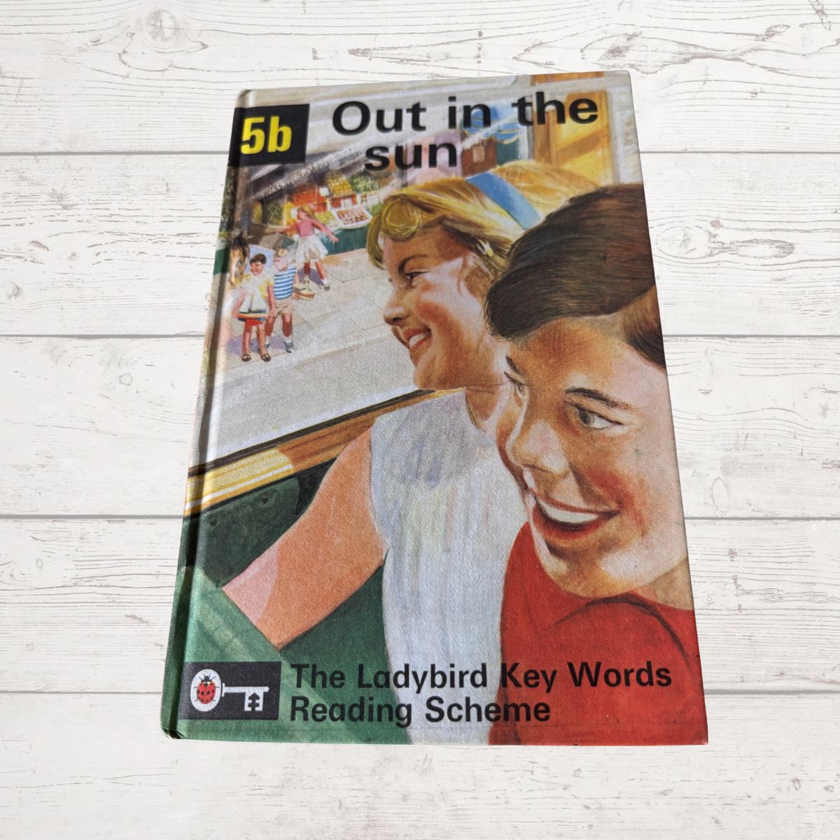 Book titled 'Out in the Sun' from The Ladybird Key Words Reading Scheme on a wooden surface