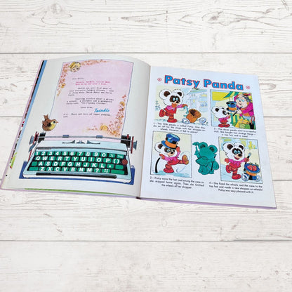 An open children's book laid flat on a white wood surface, showing printed pages with a typewriter illustration and cartoon panels titled 'Patsy Panda.'.