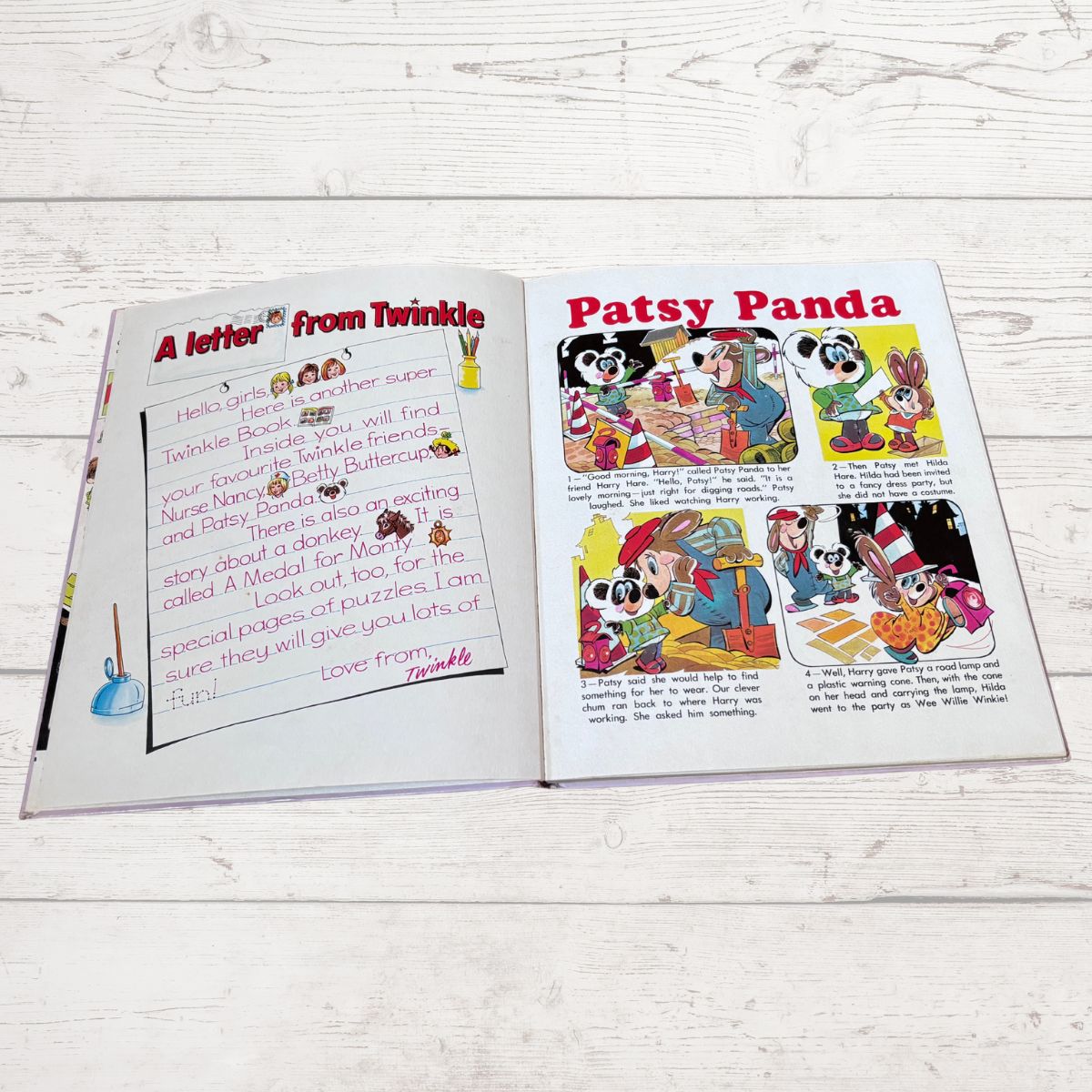 An open children's book or activity booklet laid flat on a white wood surface, showing two printed pages with cartoon illustrations and handwritten text.