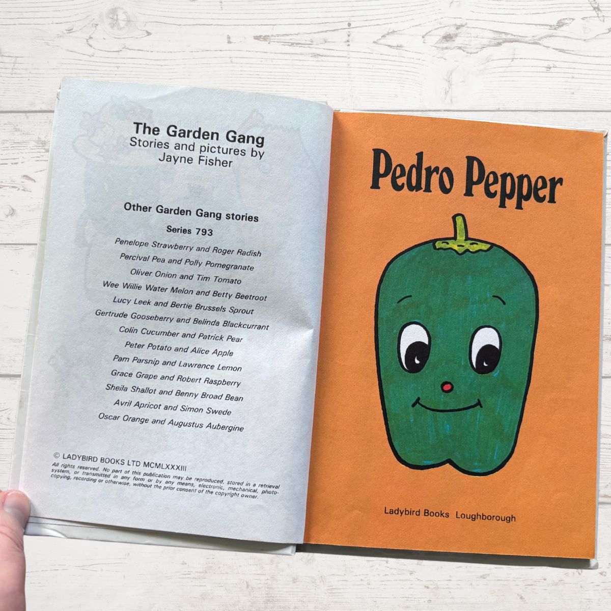 Open book showing the title page with a cartoon green pepper character on an orange background.