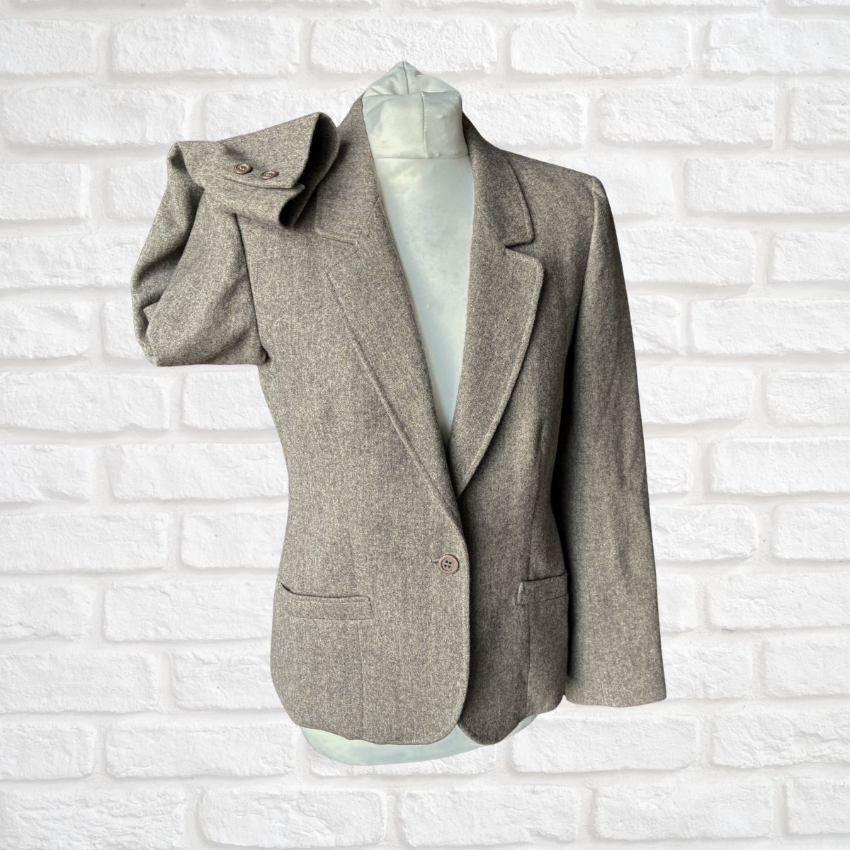 Gray /brown blazer on a mannequin against a white brick wall background