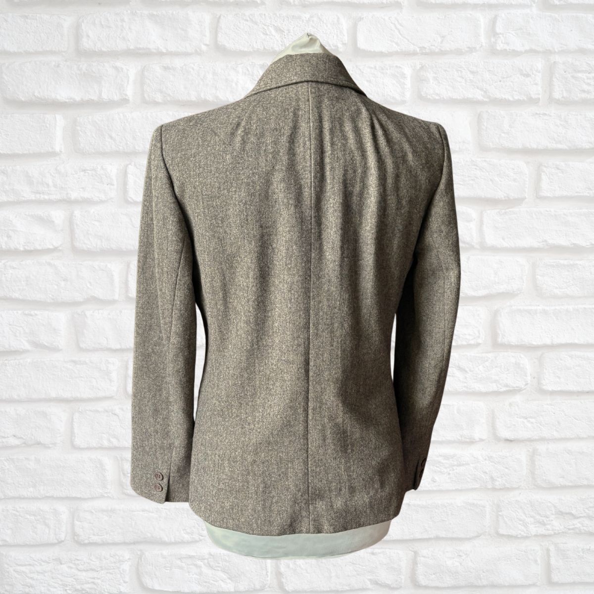 Gray blazer on a mannequin against a white brick wall background