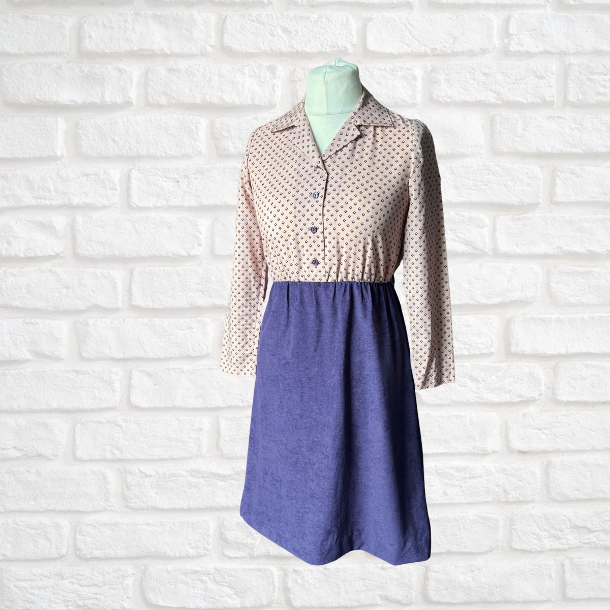 Mannequin wearing a dress with a geometric print top and purple skirt  against a white brick wall