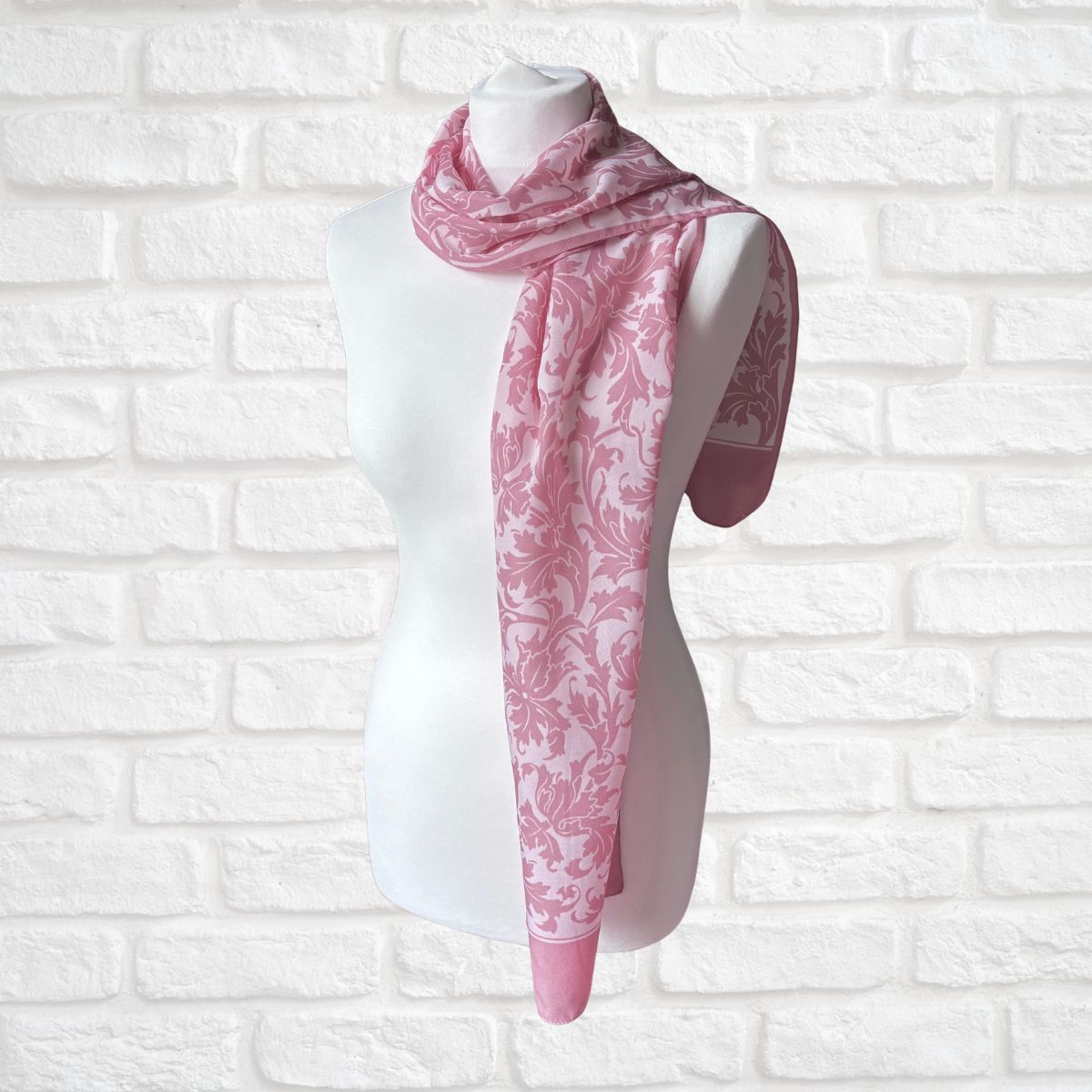 Mannequin wearing a pink and white patterned scarf against a white brick wall.