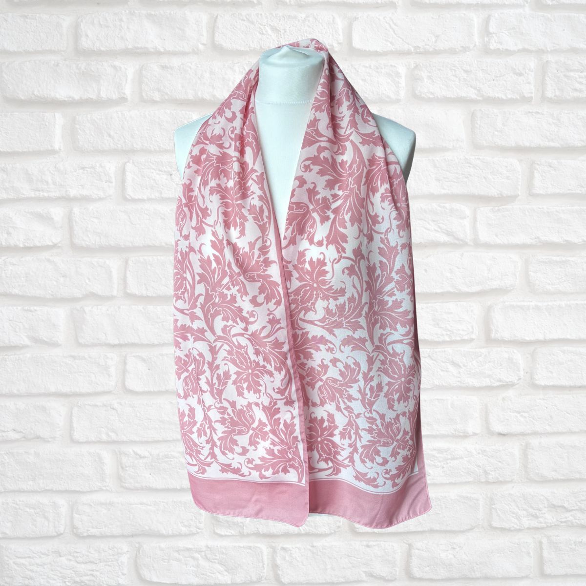 Pink and white patterned scarf on a mannequin against a white brick wall.