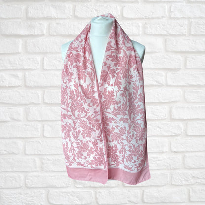 Pink and white patterned scarf on a mannequin against a white brick wall.