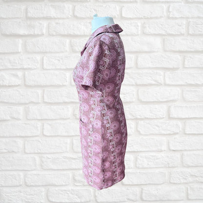 A short-sleeve collared dress  in a pink and purple paisley pattern, displayed on a mannequin torso against a white brick wall background.