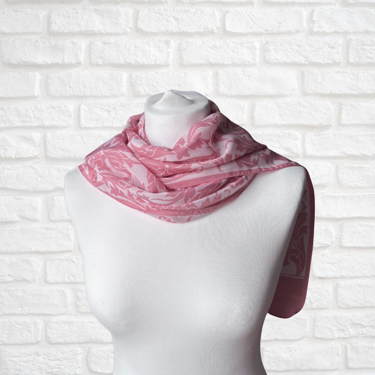 Mannequin wearing a pink and white patterned scarf against a white brick wall.