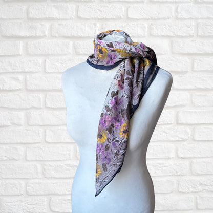 Floral scarf draped over a mannequin head against a white brick wall.