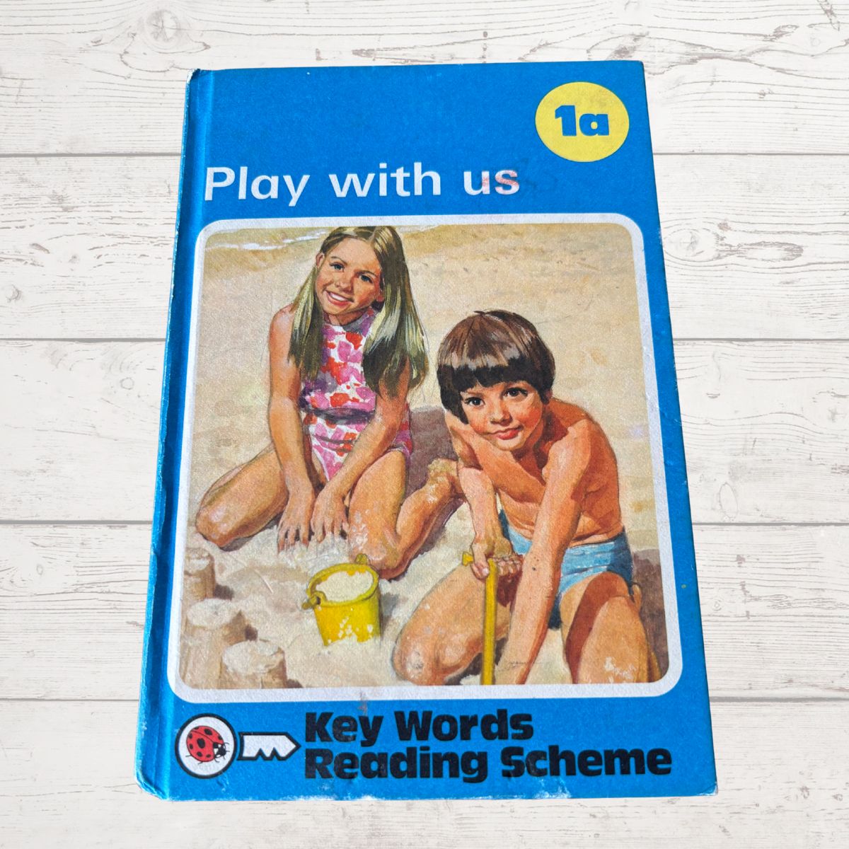 Book titled 'Play with us' from Key Words Reading Scheme on a wooden surface