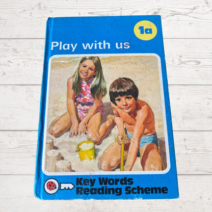 Book titled 'Play with us' from Key Words Reading Scheme on a wooden surface