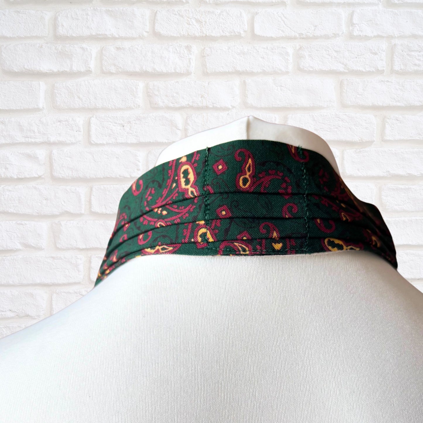 Green neck tie with red and yellow pattern on a mannequin head against a white brick wall.