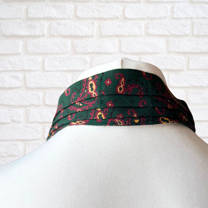 Green neck tie with red and yellow pattern on a mannequin head against a white brick wall.