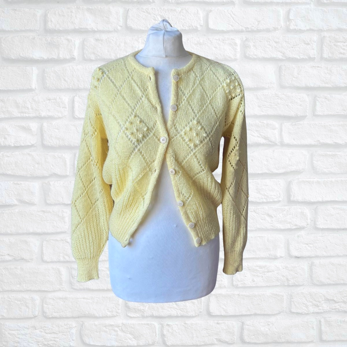 Yellow knitted cardigan on a mannequin against a white brick wall background