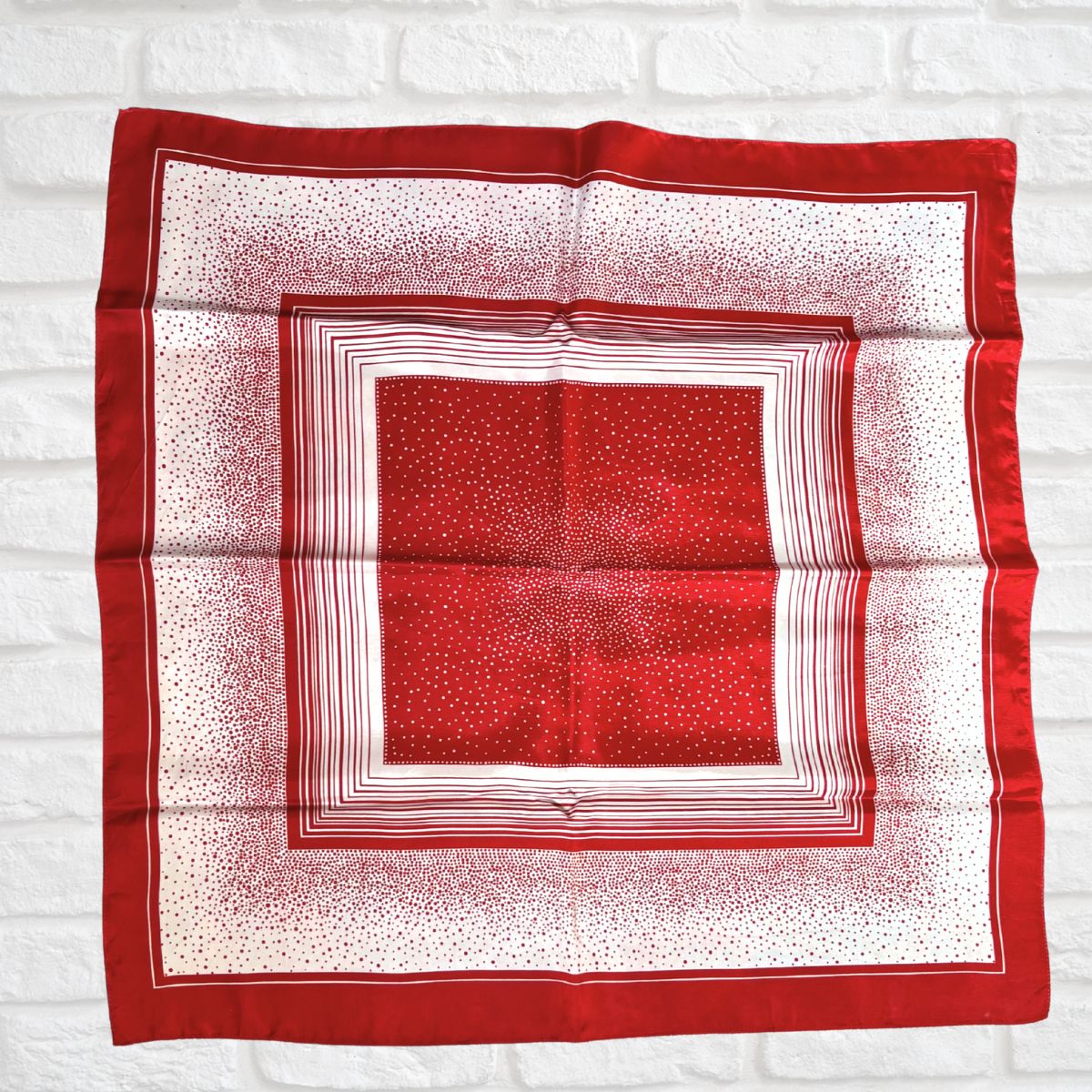 Red and white patterned square scarf on a white brick wall background
