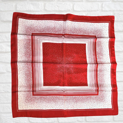Red and white patterned square scarf on a white brick wall background