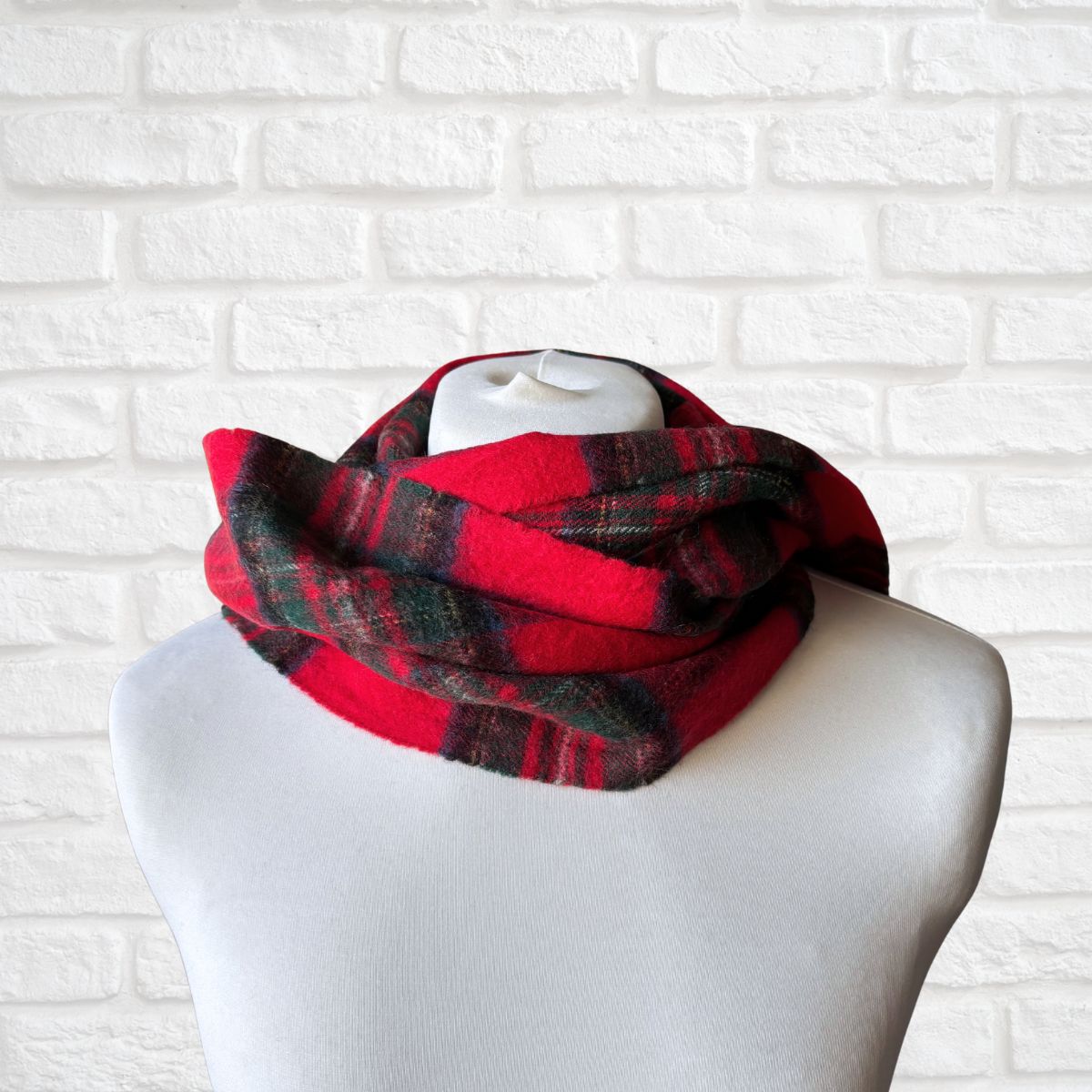 Red and green plaid scarf on a mannequin against a white brick wall background