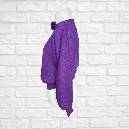 A purple knit sweater displayed on a white mannequin torso against a white brick wall background.