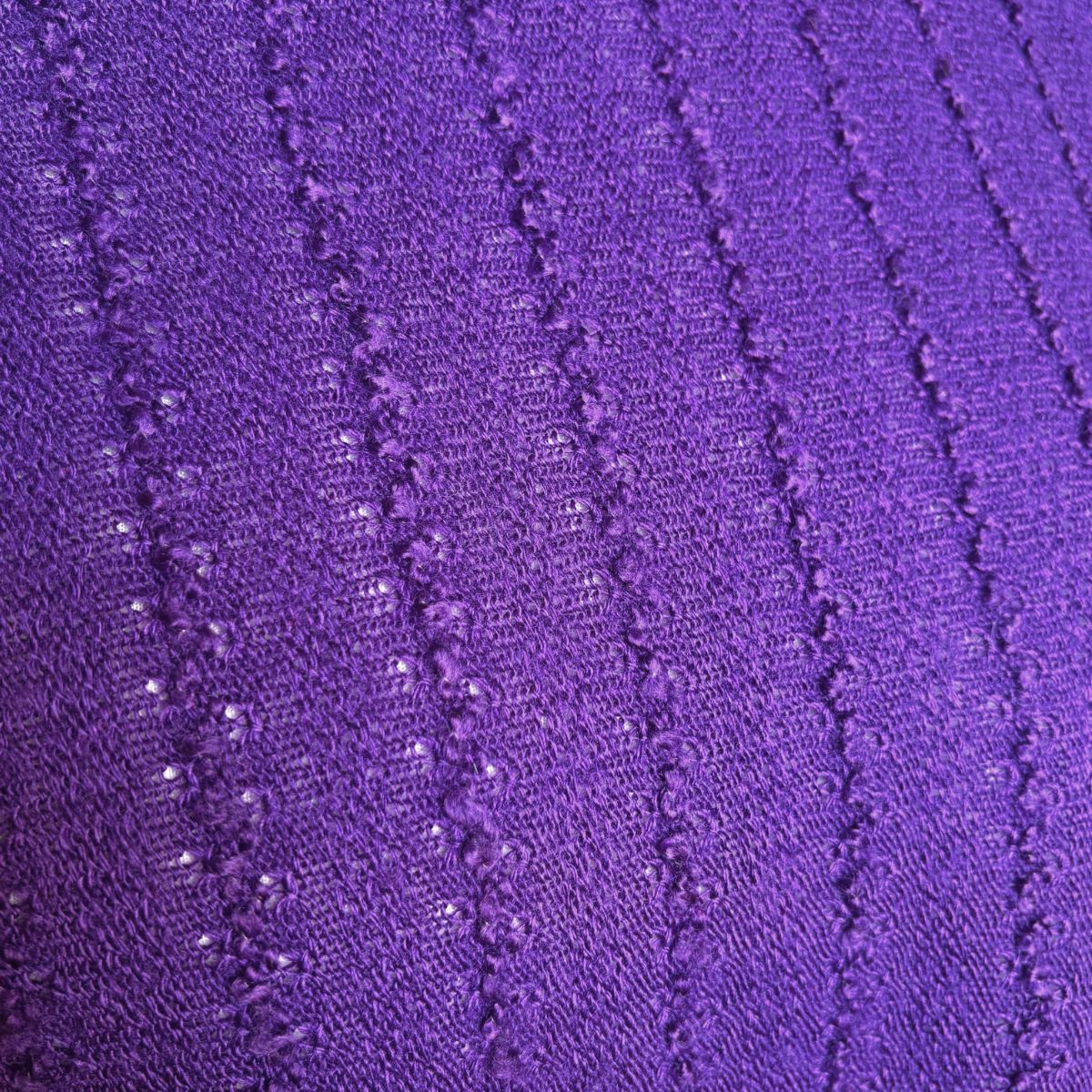 A close-up of a purple knit fabric with a textured vertical ribbed pattern.