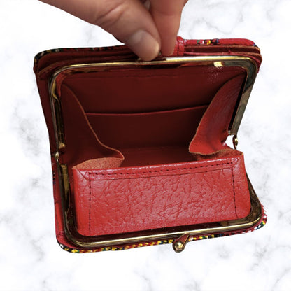 Red leather wallet with gold trim held open by a hand on a white background