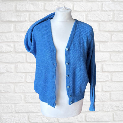 A bright blue knit cardigan sweater with a hood and front buttons, displayed on a white mannequin torso against a white brick wall background.