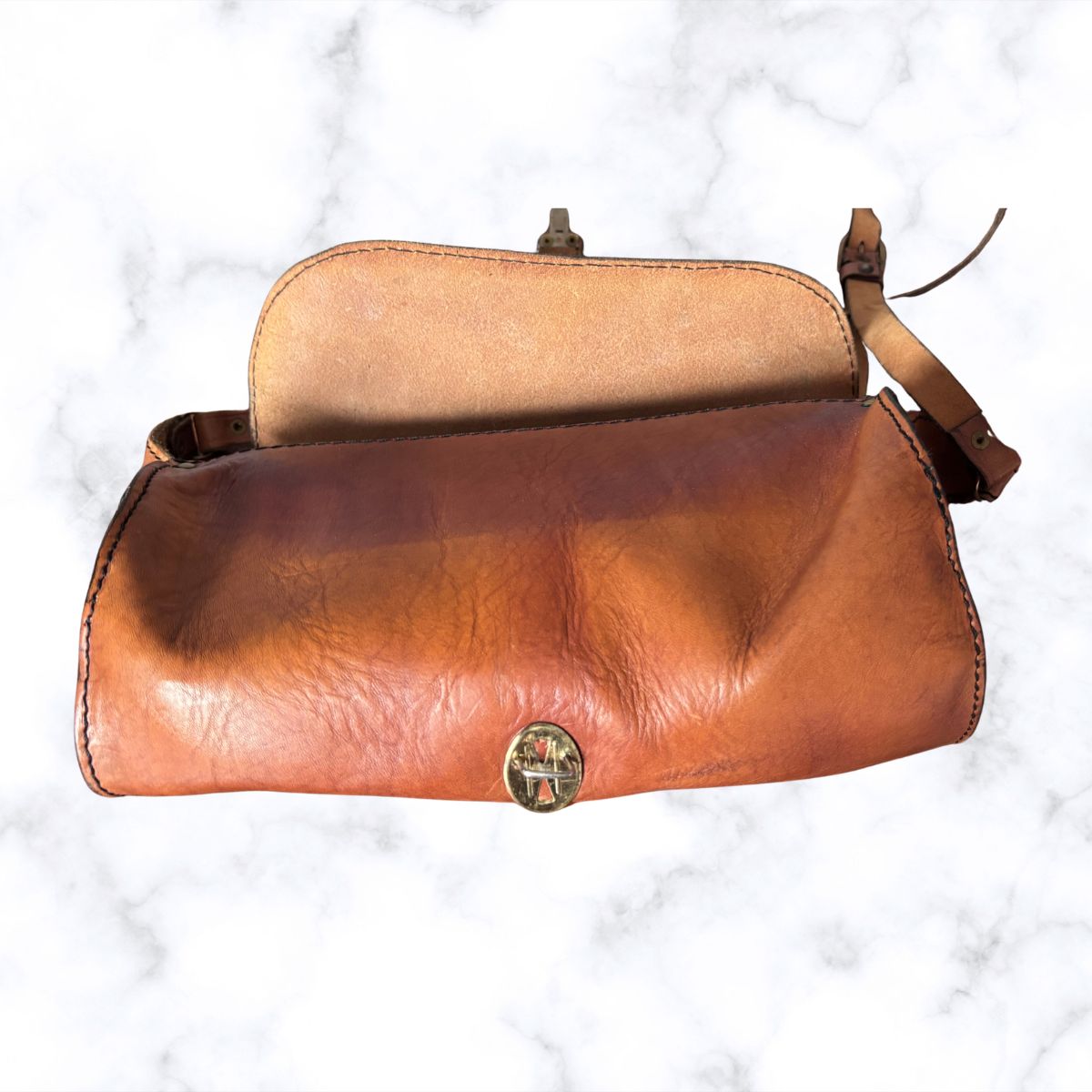 A vintage leather shoulder bag with a warm brown gradient exterior, a tan interior lining, and a small round metal clasp, displayed on a white marble background.