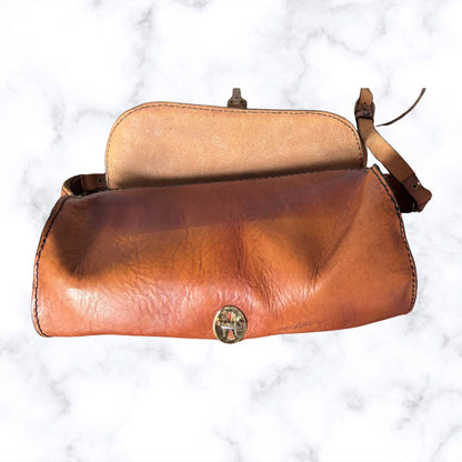 A vintage leather shoulder bag with a warm brown gradient exterior, a tan interior lining, and a small round metal clasp, displayed on a white marble background.