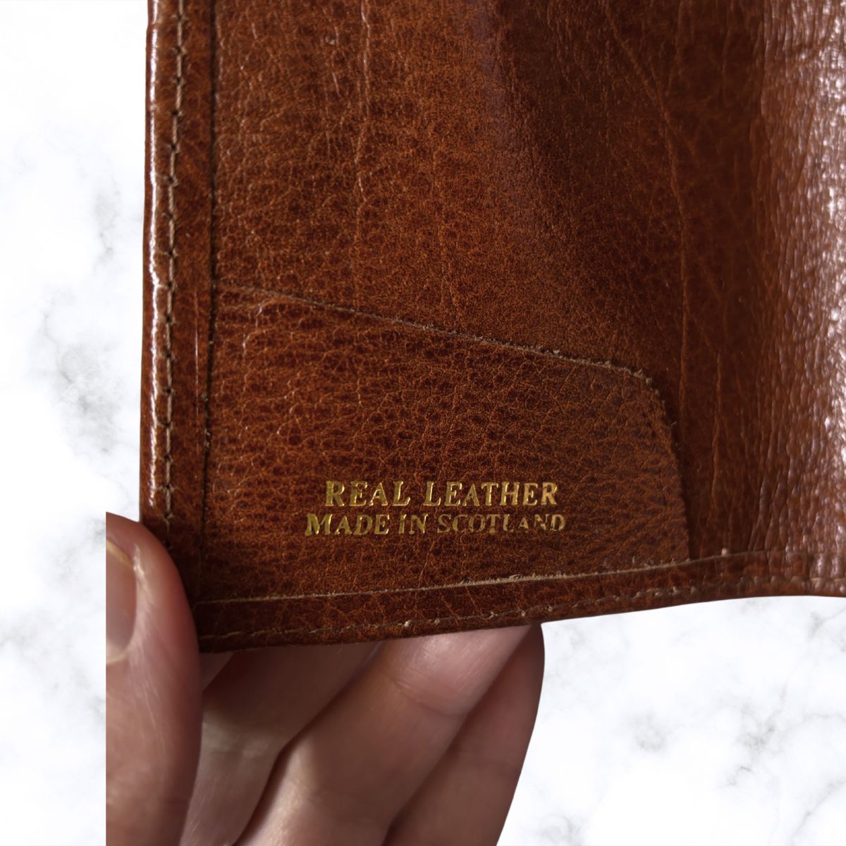 Brown leather wallet with 'Real Leather Made in Scotland' text held by a hand on a white background