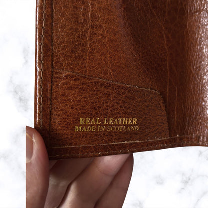 Brown leather wallet with 'Real Leather Made in Scotland' text held by a hand on a white background