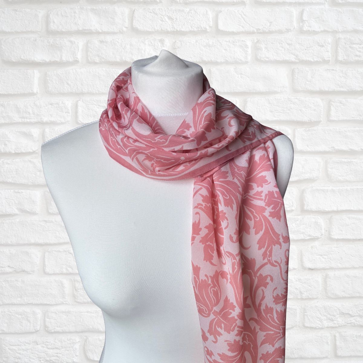 Pink and white patterned scarf on a mannequin against a white brick wall.