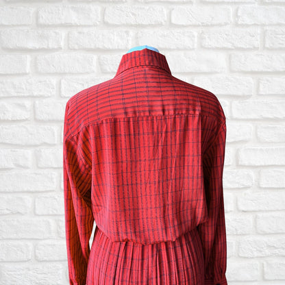 A red long-sleeve collared shirt dress with a black windowpane plaid pattern, shown from the back on a dress form against a white brick wall background.