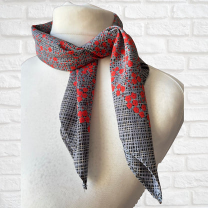 Scarf with red poppy and black pattern draped over a mannequin against a white brick wall.