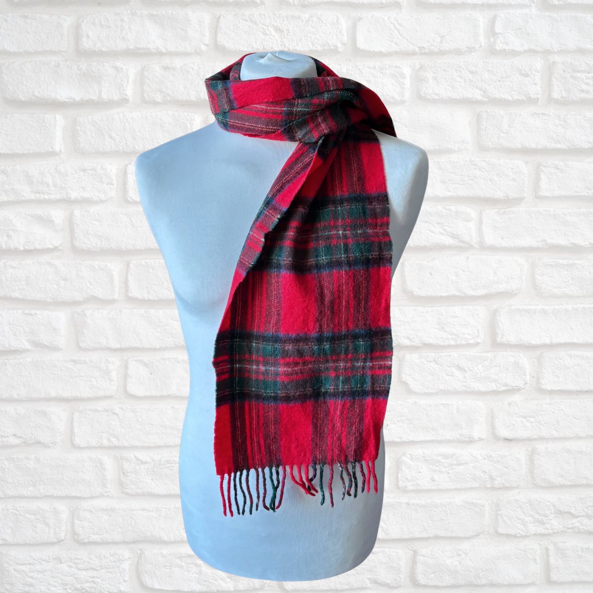 Red and black plaid scarf on a mannequin against a white brick wall.
