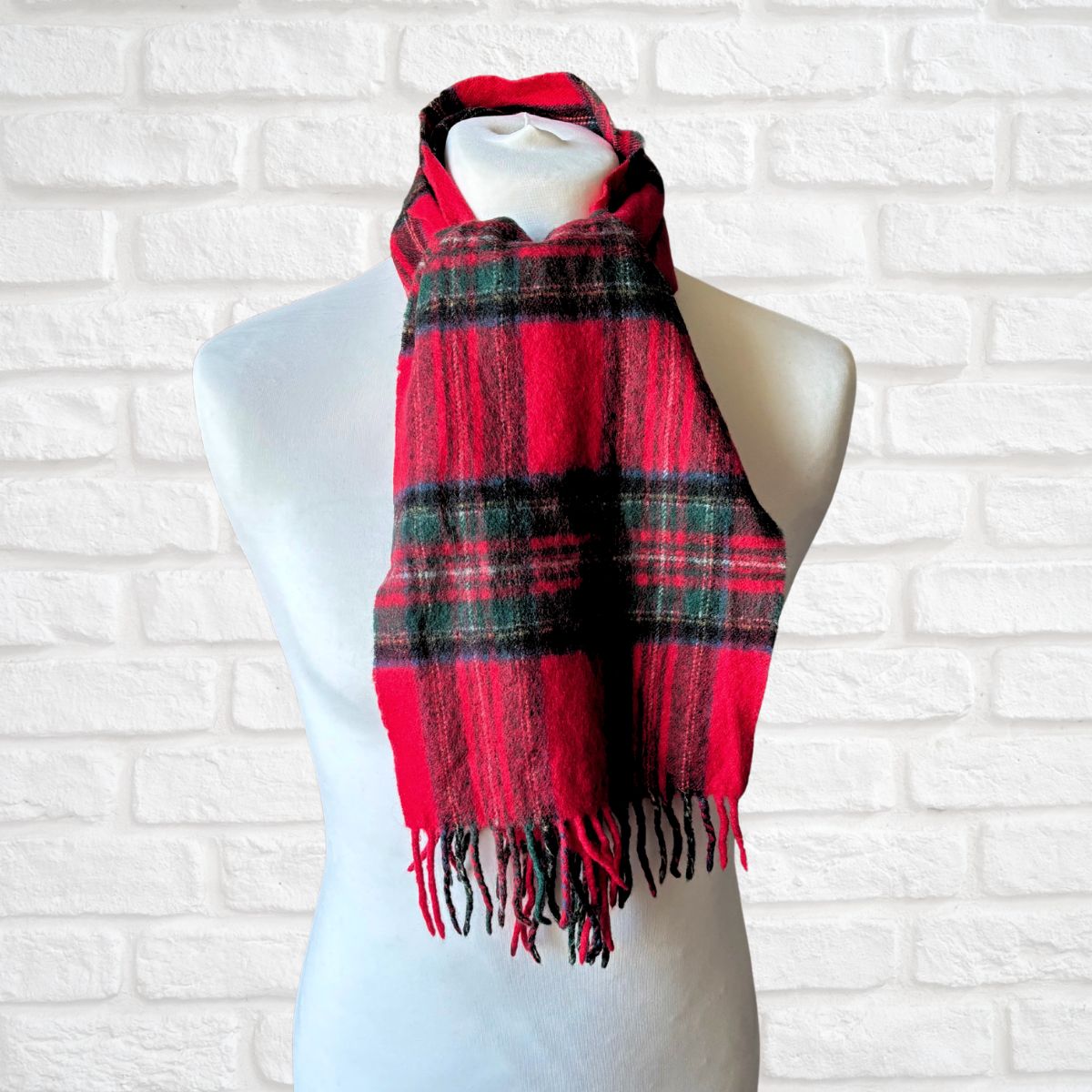 Red and black plaid scarf on a mannequin against a white brick wall.