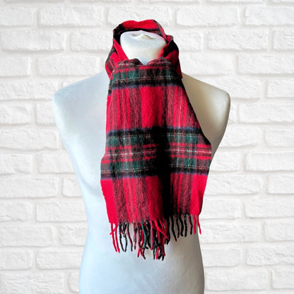 Red and black plaid scarf on a mannequin against a white brick wall.