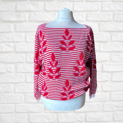 A red and white striped knit sweater with red floral motifs, displayed on a white mannequin torso against a white brick wall background.