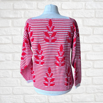 A red and white striped knit sweater with red leaf motifs, displayed on a light blue mannequin torso against a white brick wall background.