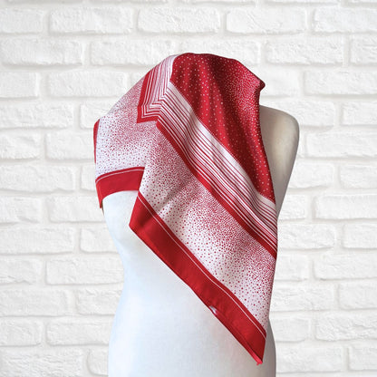 Red and white patterned scarf on a mannequin against a white brick wall background