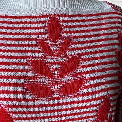 Close-up of a red and white knit sweater featuring a large red maple leaf motif over horizontal red and white stripes.